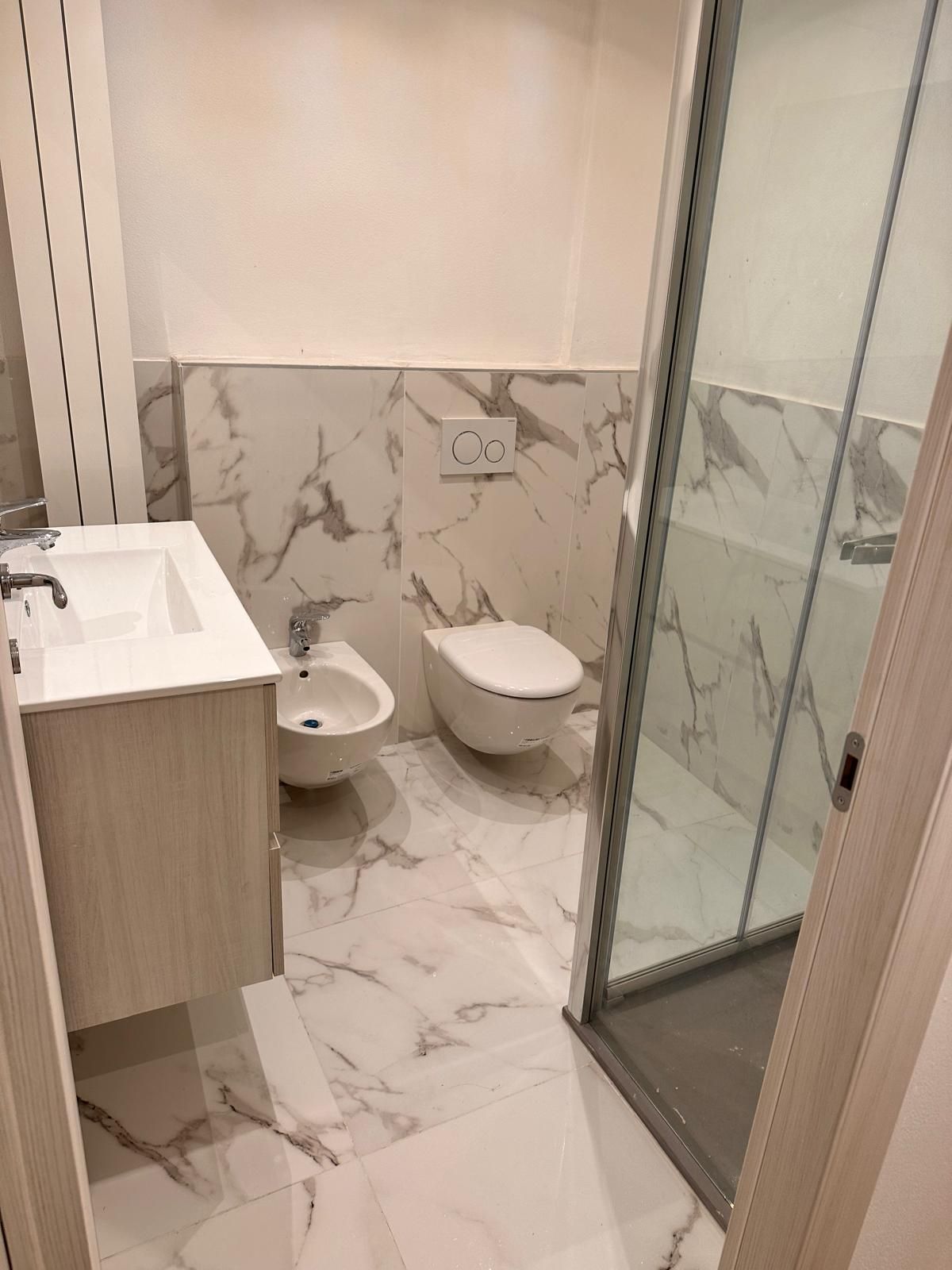 Bagno in fase di ristrutturazione, con pareti piastrellate, pavimento in piastrelle rosse, impianti idraulici a vista.