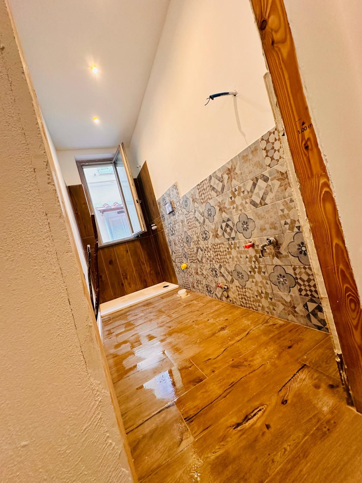 Il cane è seduto davanti a un edificio in pietra con una porta di legno, un ingresso ad arco e una piccola finestra con sbarre di metallo.