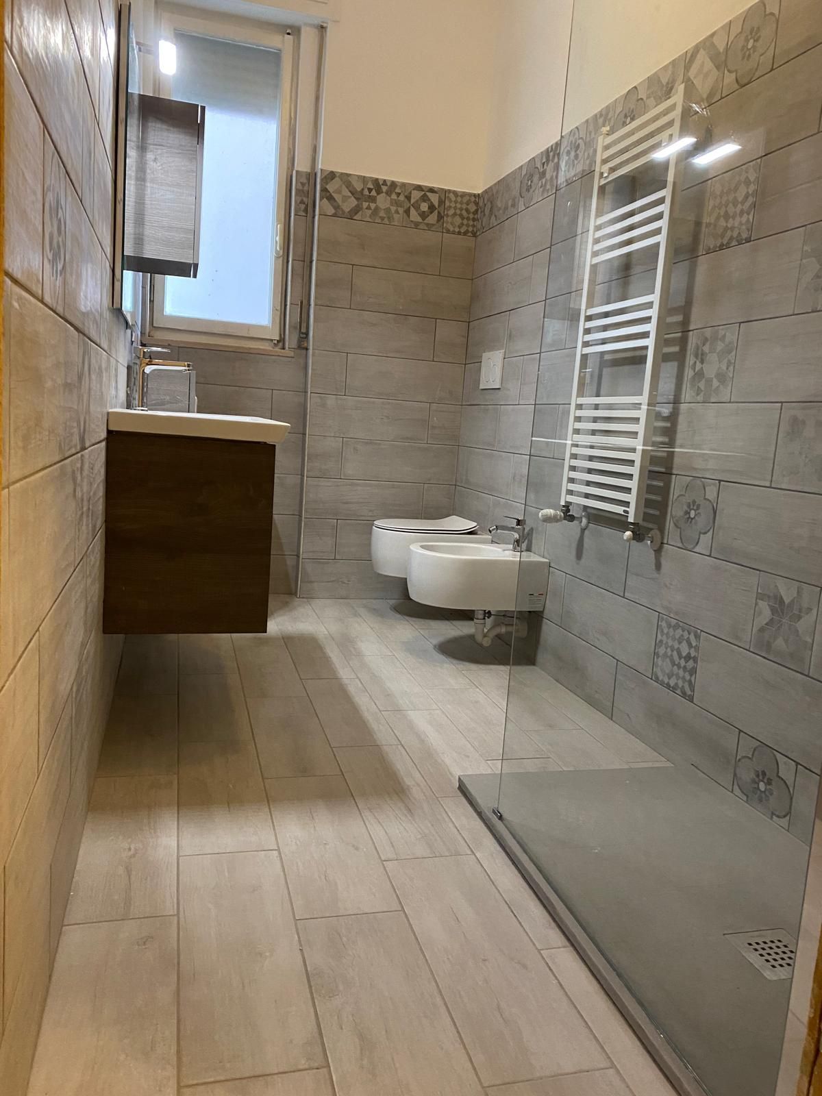 Bagno con pareti e pavimento piastrellati grezzi; è installato un piatto doccia.