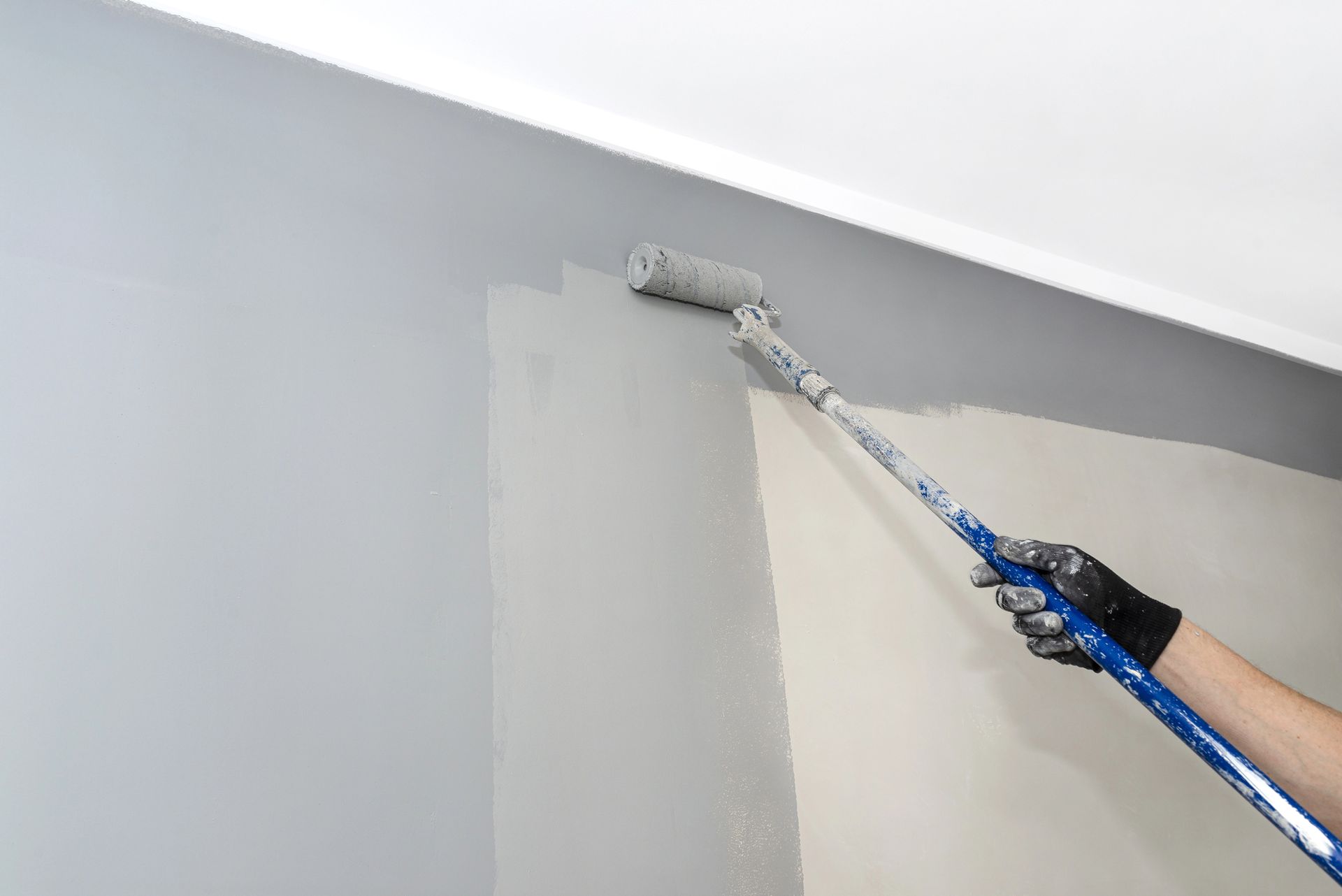 Persona che dipinge un muro di grigio con un rullo.