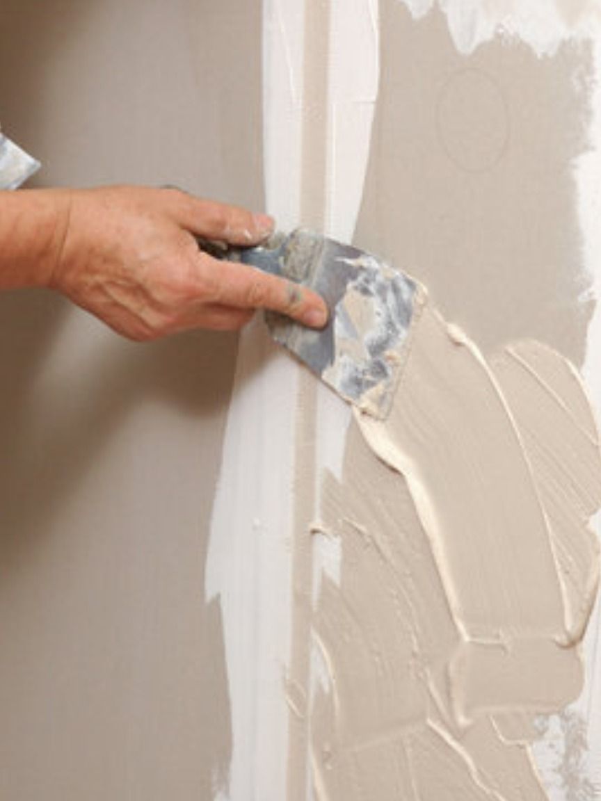 Hand with a putty knife applying drywall compound to a seam on a wall.