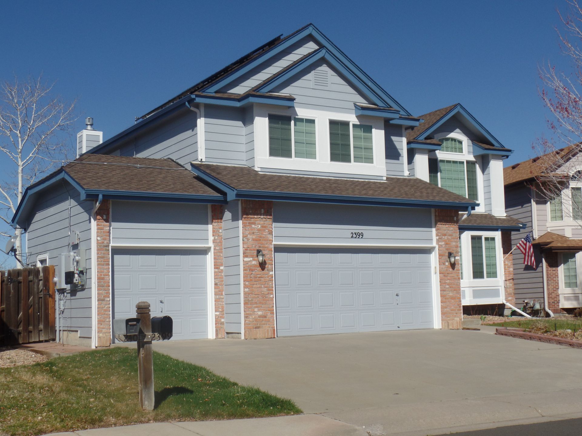 A two-story suburban house with light blue siding, brick accents, a two-car garage, and a brown shingled roof.