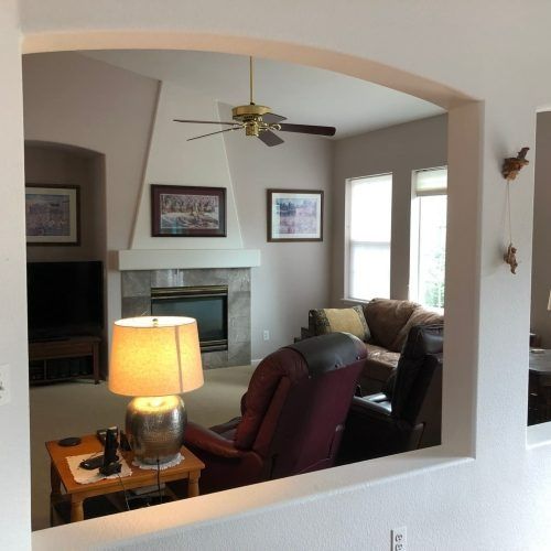 Living room seen through arched doorway; fireplace, recliner, couch, lamp, artwork, and windows.