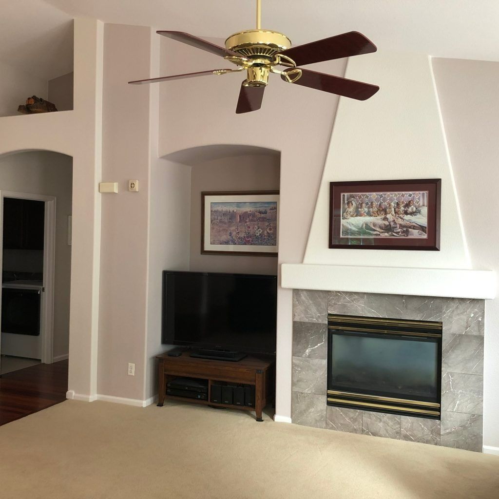 Living room with fireplace, TV, and ceiling fan. Beige carpet, gray fireplace tile, artwork.