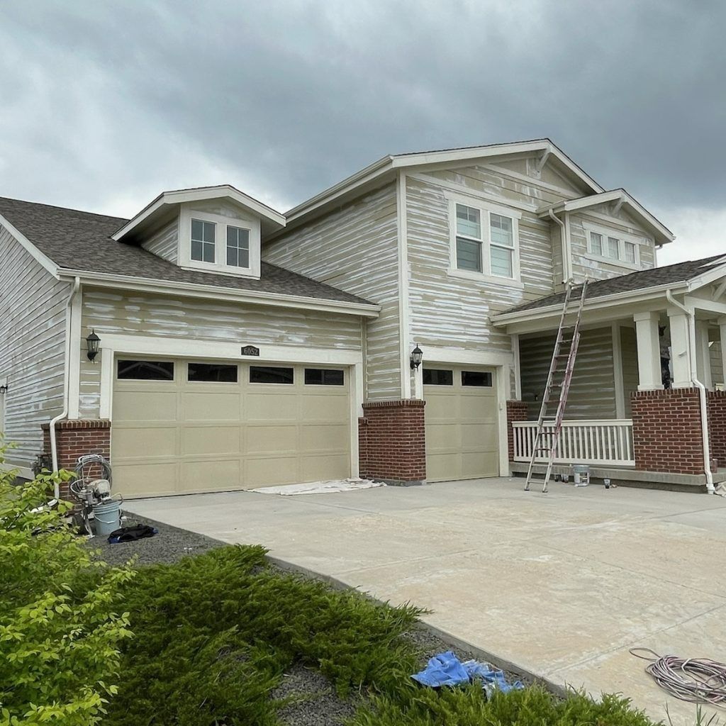 A house under renovation with light-colored siding, a two-car garage, and a ladder leaning against the second story.