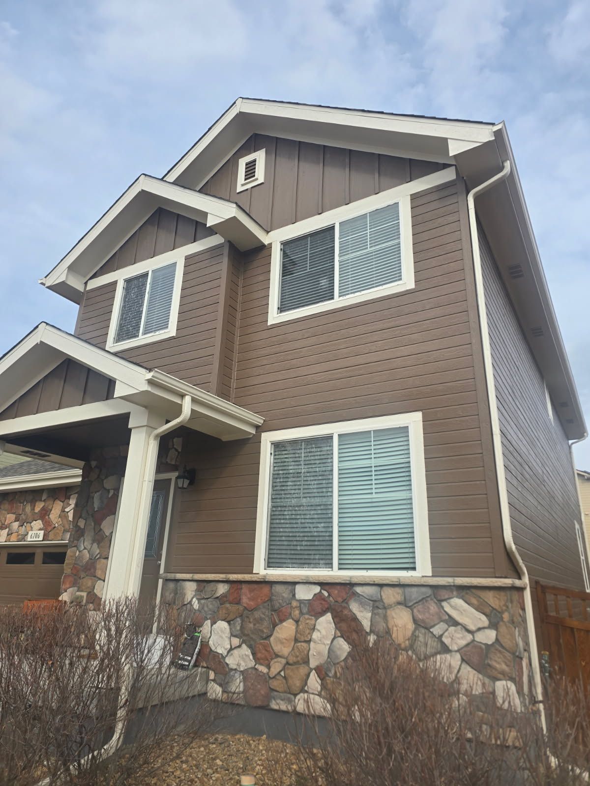 House exterior with stone facade, teal garage doors, and a person painting on a ladder.