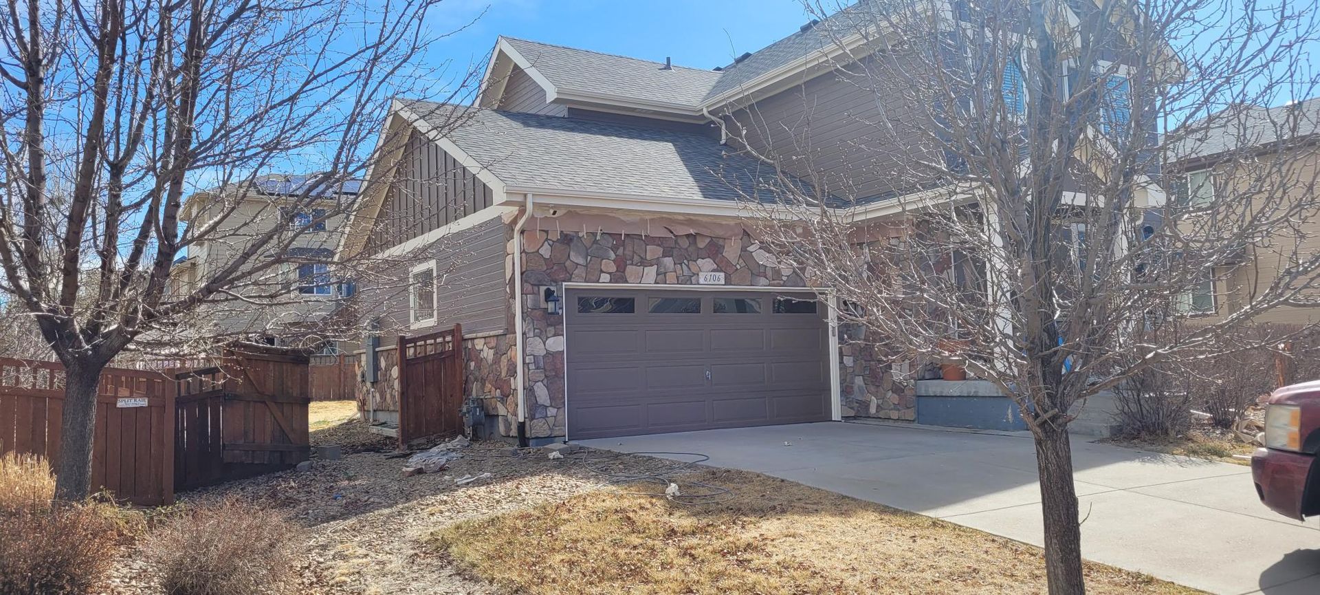 A two-story suburban house with stone siding, a dark garage door, a paved driveway, and trees on a sunny day.