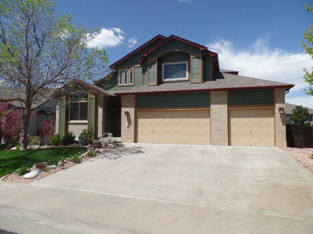 Two-story house with green siding, tan garage doors, and a concrete driveway on a sunny day.