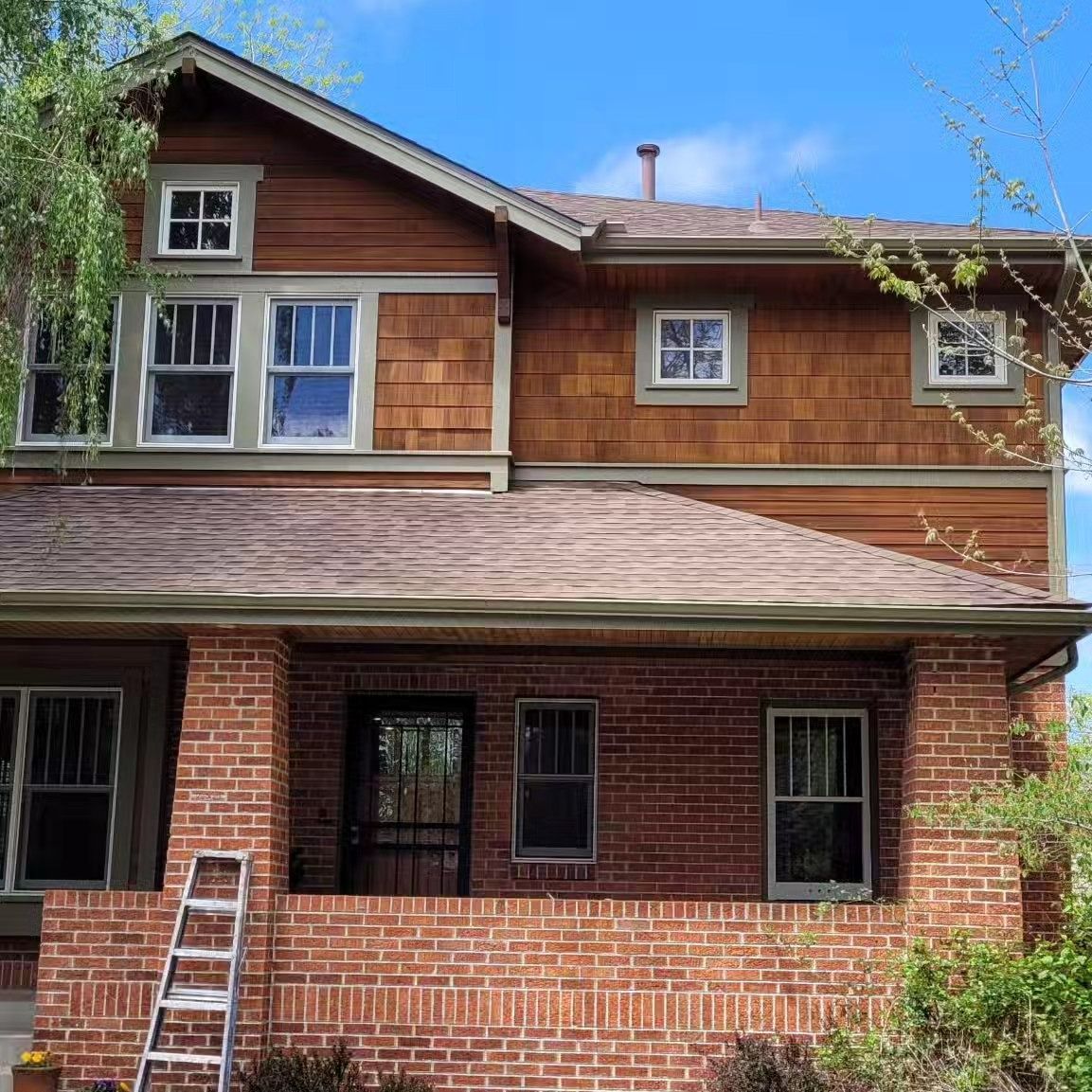 Two-story house with brick base and wood siding. Ladder leans against the brick porch.