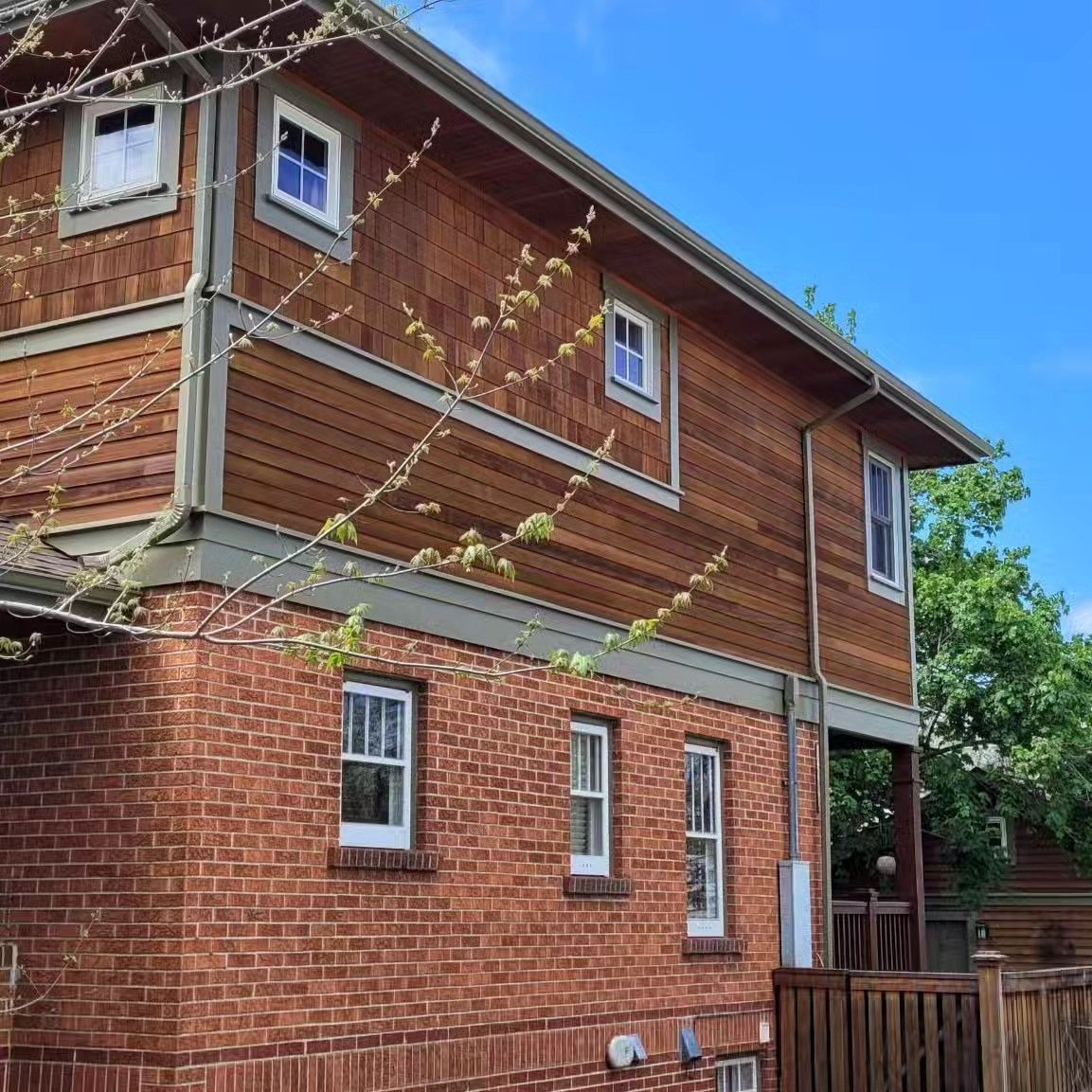 Brick house with cedar siding, white windows, and green trim against a blue sky.