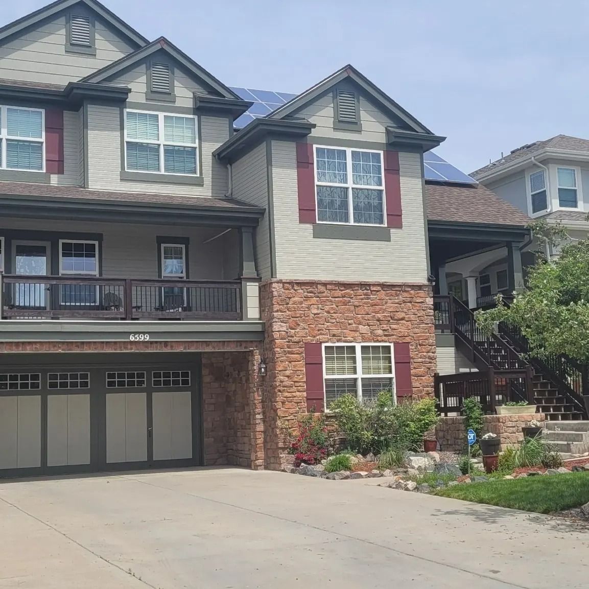 Two-story house with tan siding, brown stone, and red shutters, a garage, and a balcony.