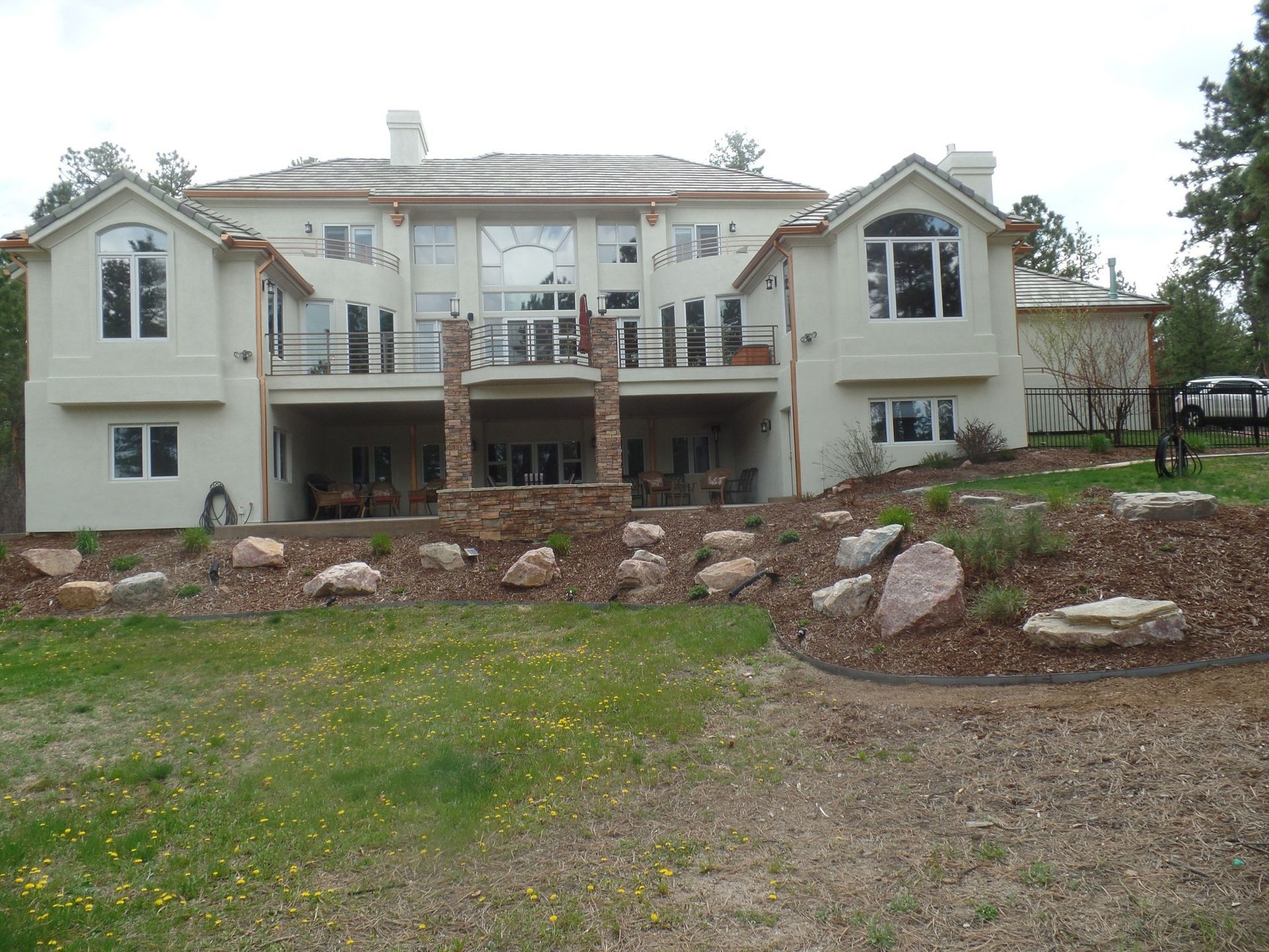 Large beige house with multiple windows, balconies, and a stone facade.