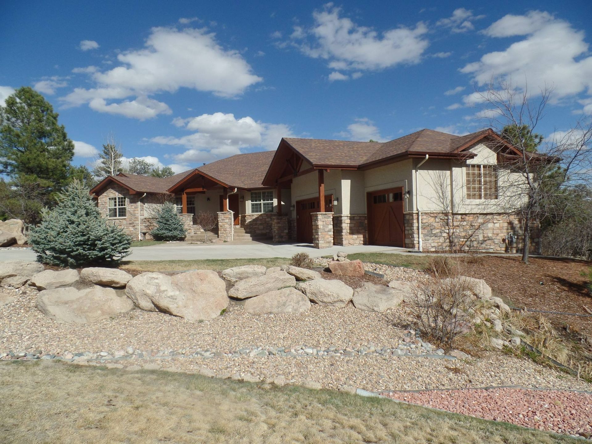 A house with a stone and tan exterior, brown roof, and a blue sky.