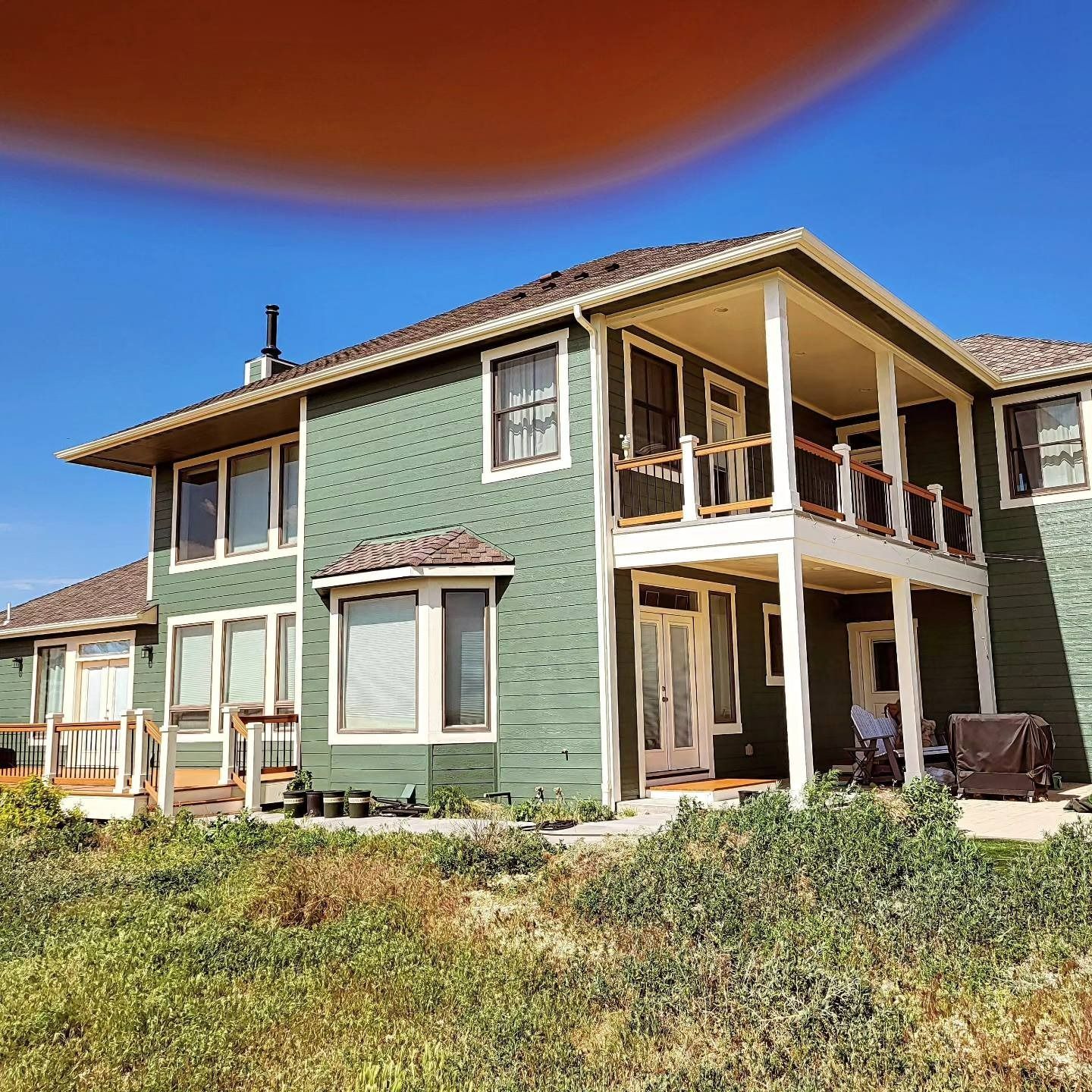 Two-story green house with covered porch, white trim, and a lawn.