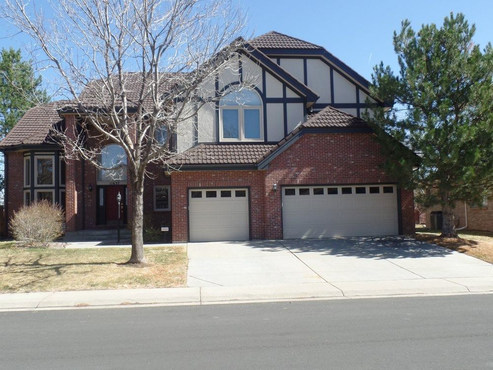 Two-story brick house with a tan garage, black trim, and a curved window above the front door.