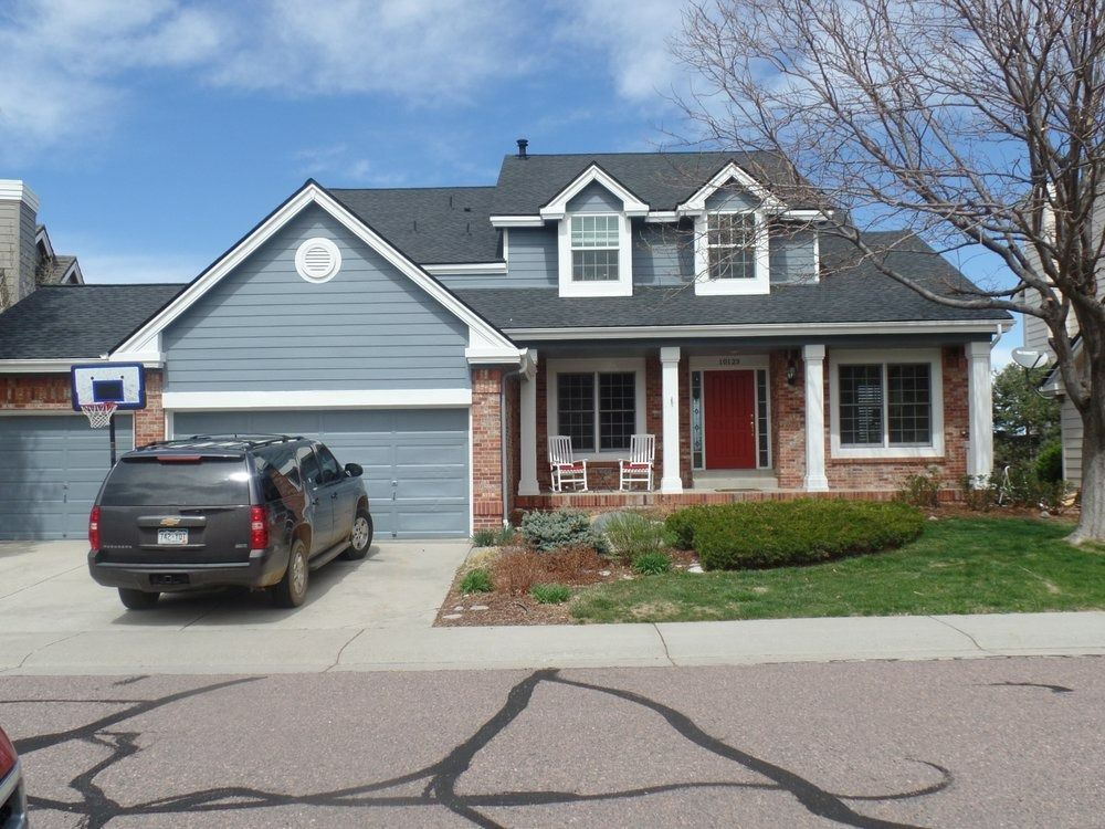 Blue house with red door, brick accents, and a gray SUV parked in the driveway.