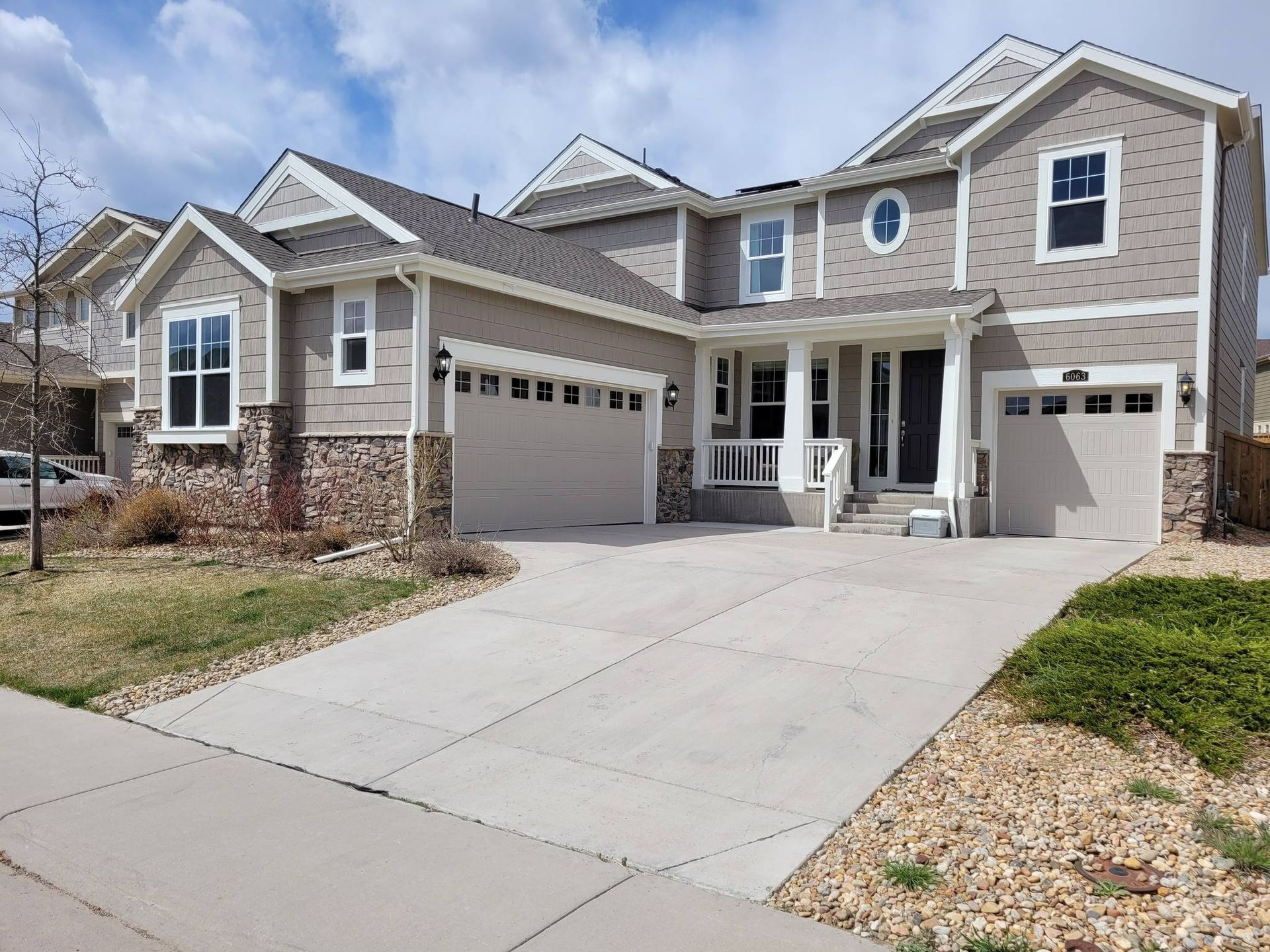 Beige two-story house with a two-car garage, stone accents, and a concrete driveway.