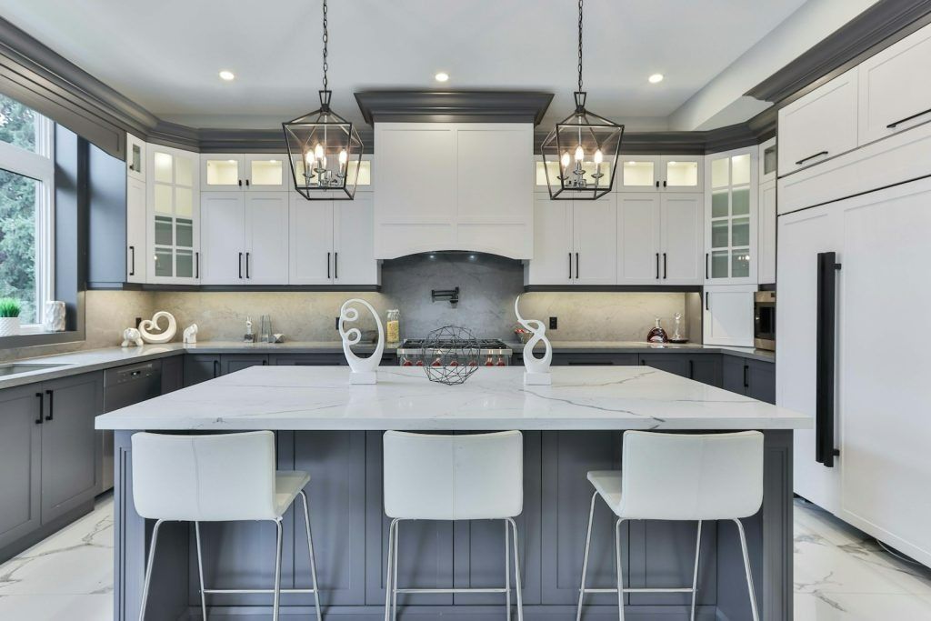 Modern kitchen with white countertops, grey cabinets, and island with white bar stools.