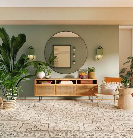 Living room with a large rug, green walls, wooden console, round mirror, and plants.