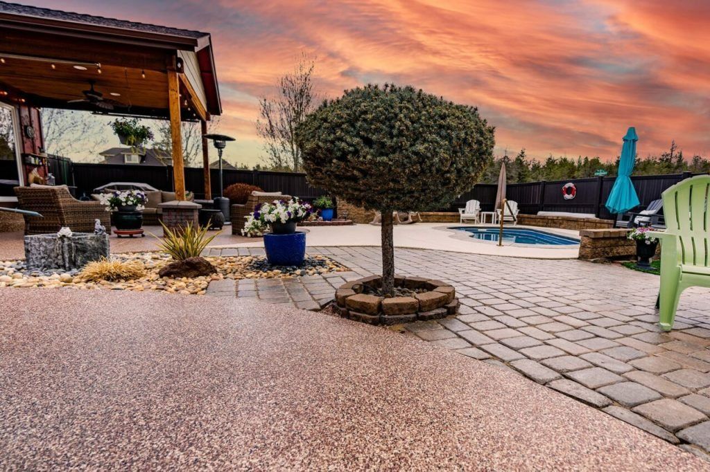 Backyard patio with pool, gazebo, and manicured tree under colorful sunset sky.