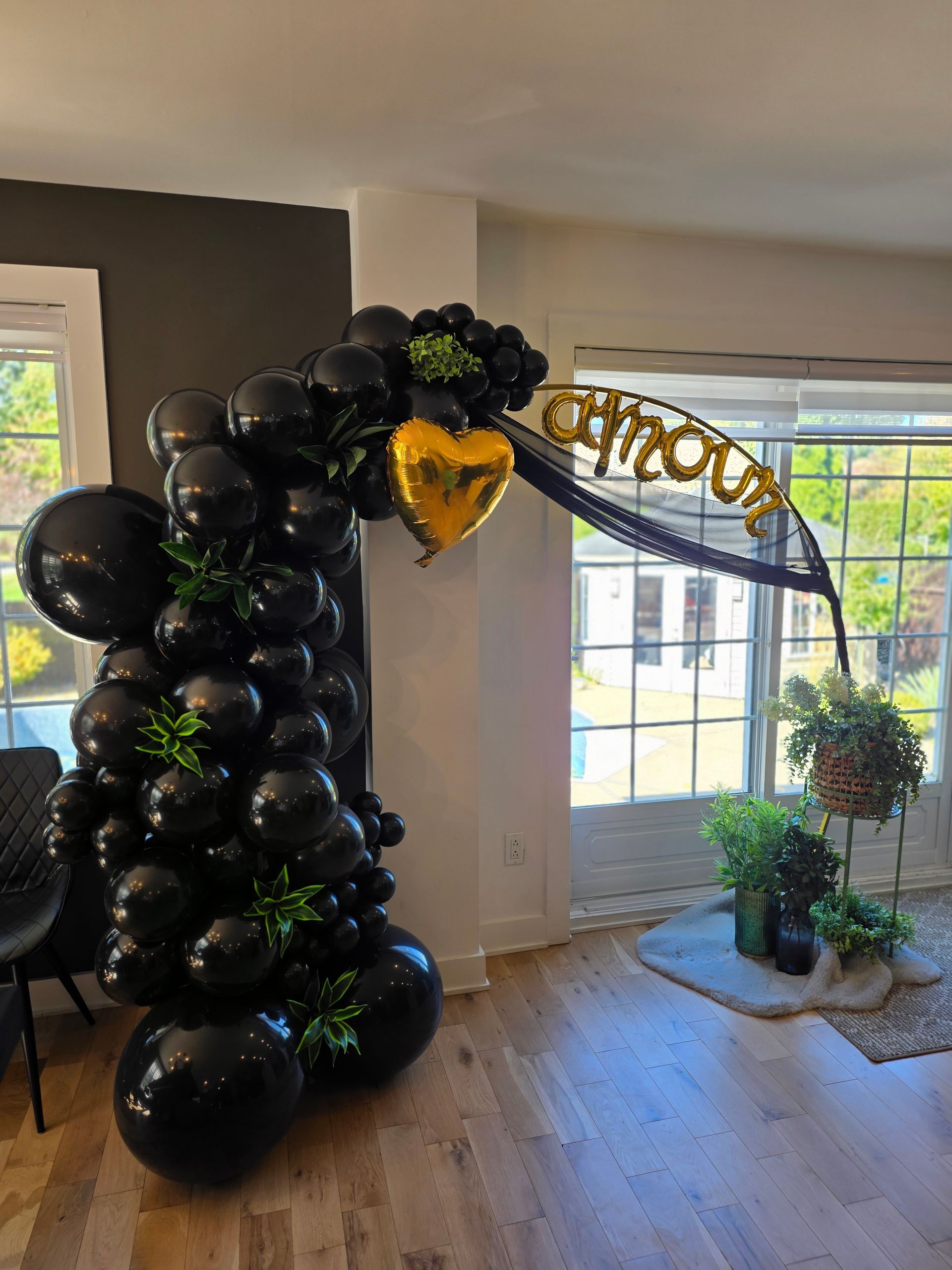 Arche de ballons noirs avec cœur doré et inscription « athour », touches de verdure.