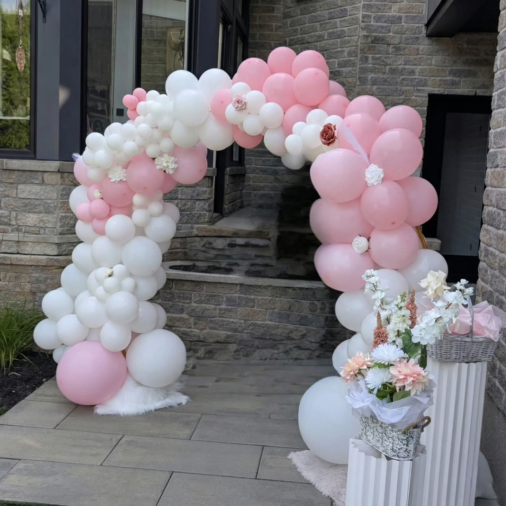 Arche de ballons roses et blancs à l'entrée ; décorations florales et marches en fausse pierre visibles.