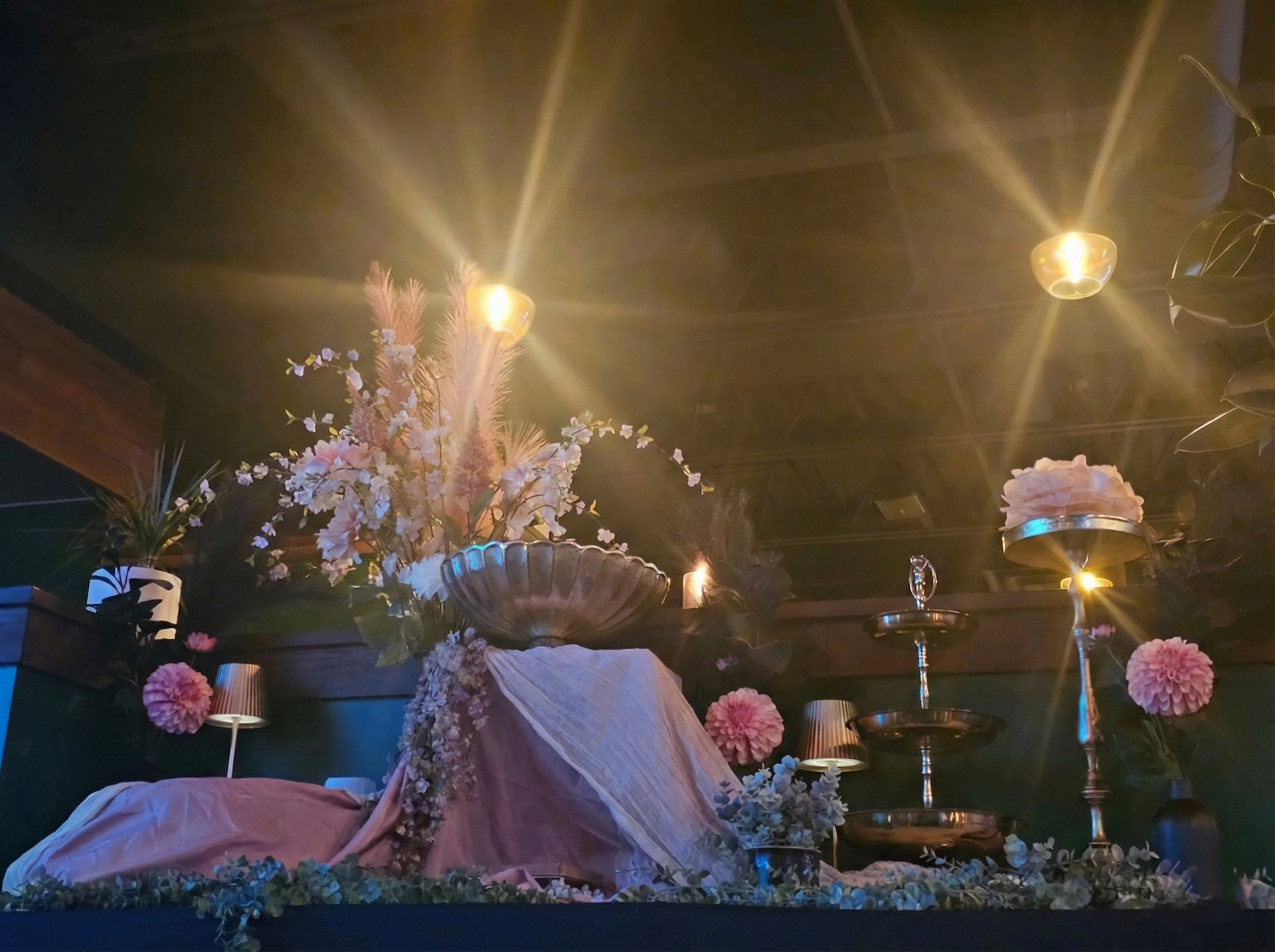 Un étalage de fleurs roses et blanches, de bougies et d'un présentoir à étages, sous une lumière chaude.