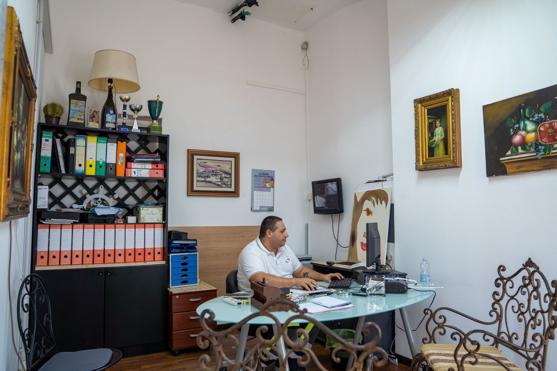 Uomo che lavora alla scrivania in un ufficio con quadri, scaffali e un computer.