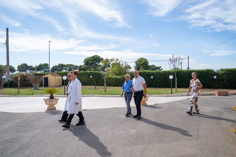 Le persone passeggiano all'aperto in una giornata di sole. Due in camice bianco, due in abiti casual.