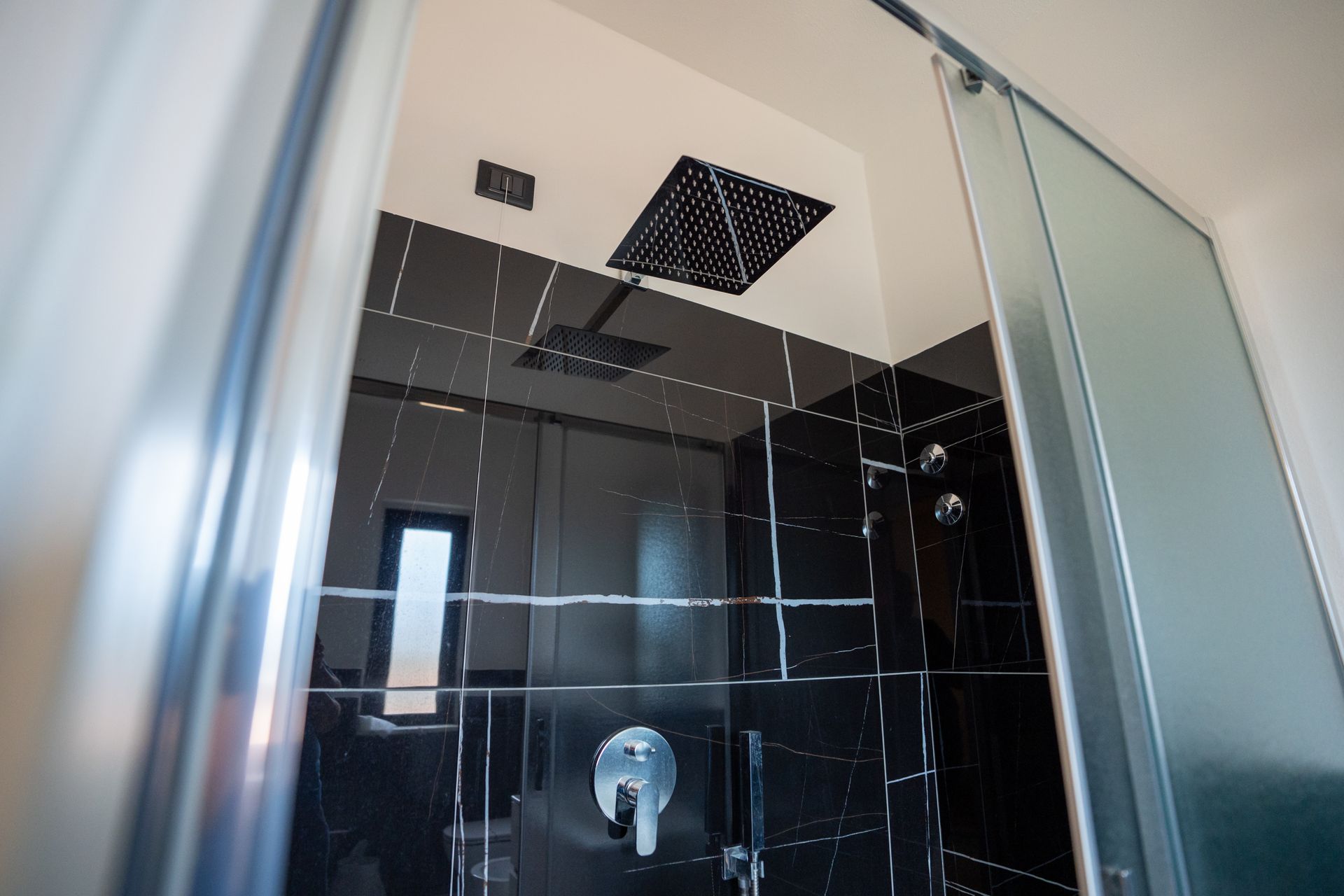 Bagno con doccia, lavabo e specchio, caratterizzato da piastrelle bianche e nere e un mobiletto in legno chiaro.