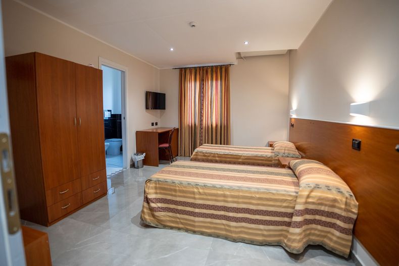 Camera d'albergo con persona, letto, scrivania, TV e fiori.