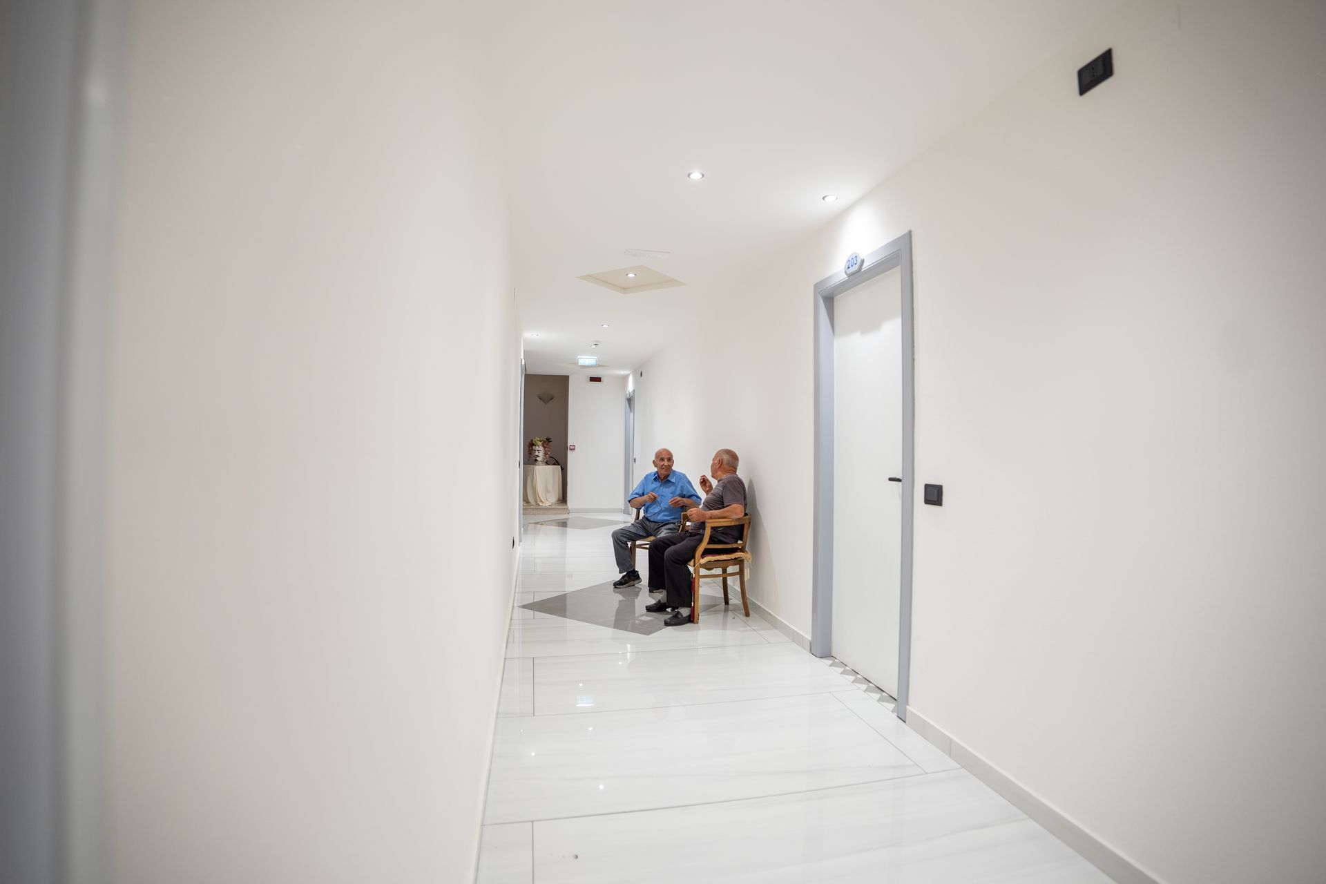 Due uomini seduti su letti separati in una stanza d'albergo arredata in modo neutro.