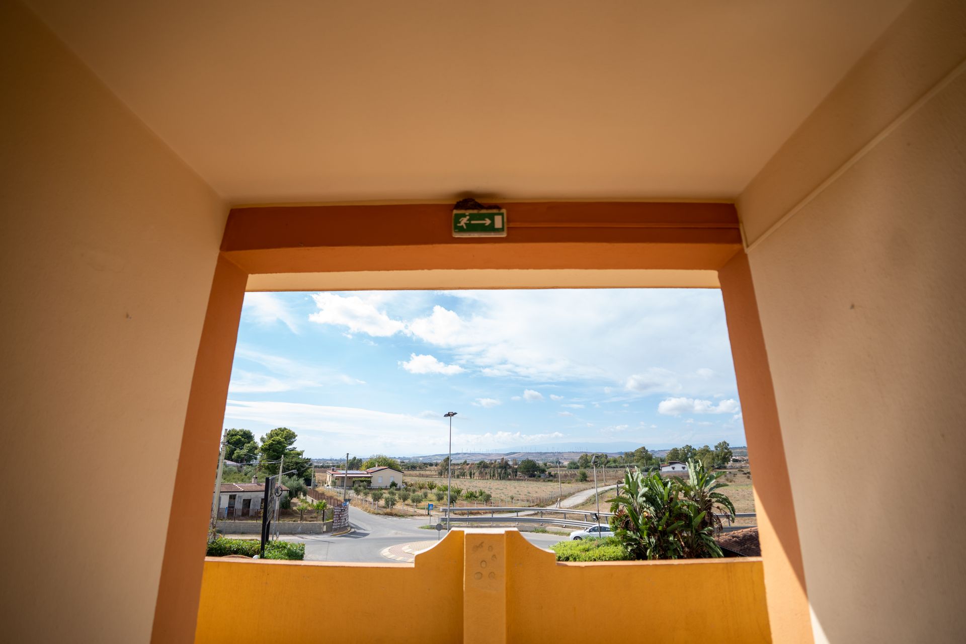 Vista da un portone arancione che domina un paesaggio con cielo azzurro e alberi.