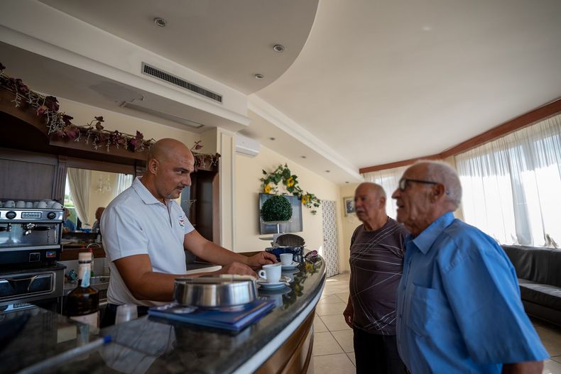 Due persone sono sedute su un divano scuro in una stanza con grandi finestre e tende trasparenti.