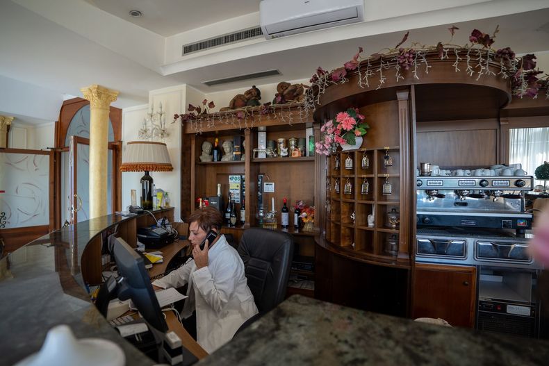 Donna alla reception al telefono, interno con macchina per il caffè, bottiglie e decorazioni floreali.