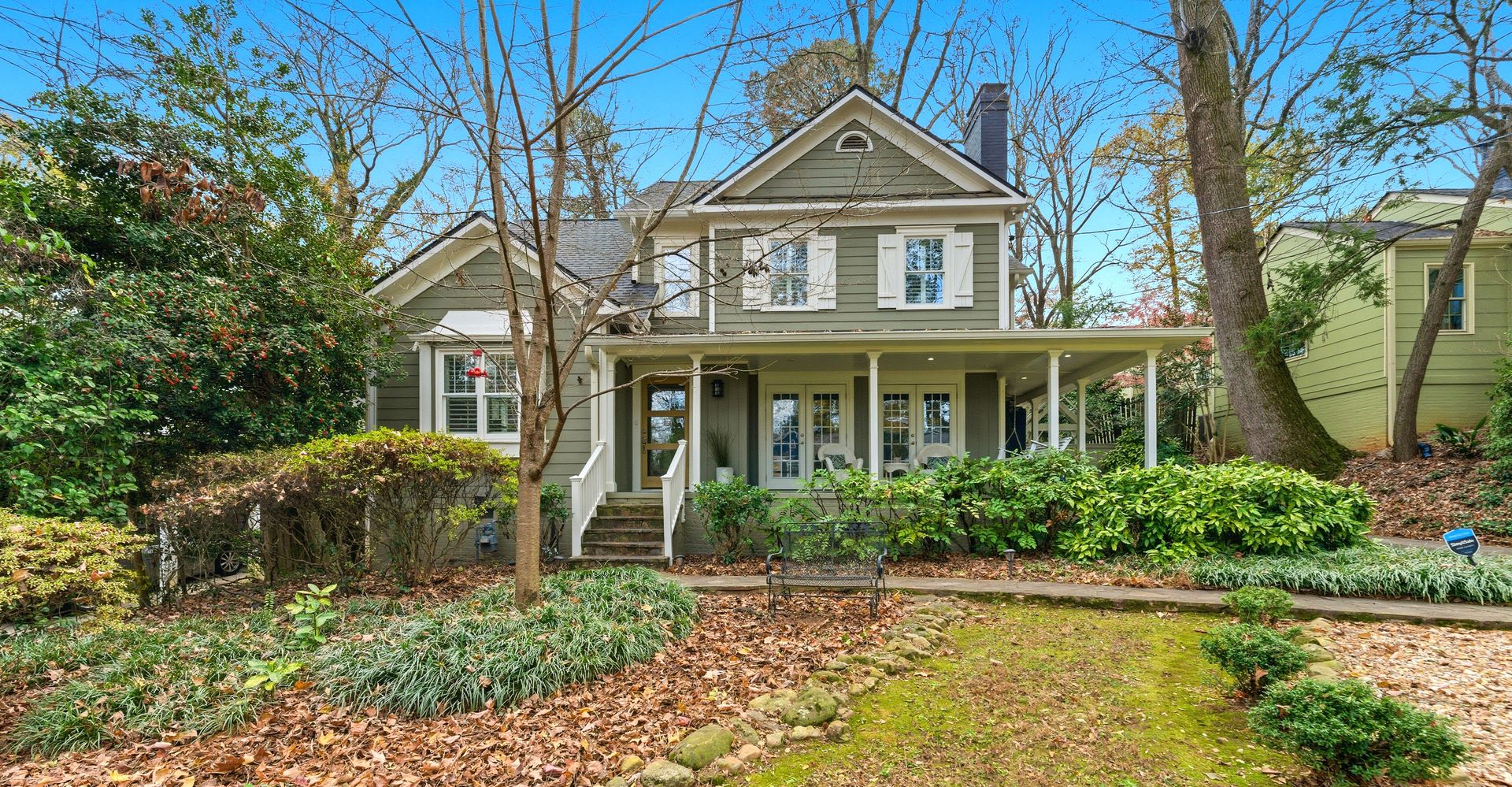 Two-story house with green siding, white trim, and a small porch, surrounded by trees and bushes.
