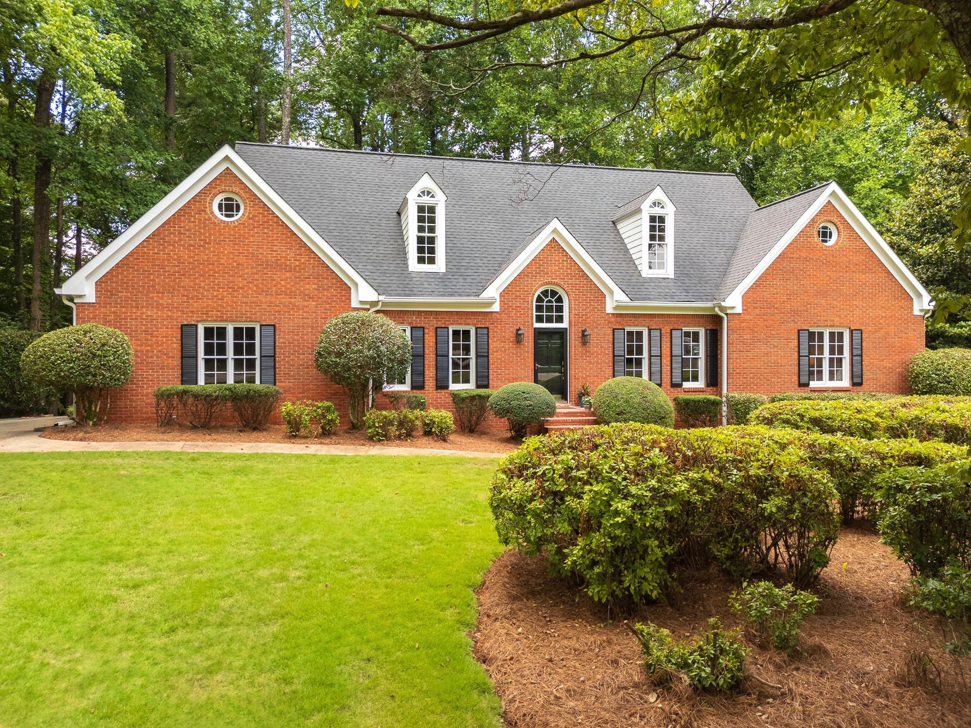 A large brick house with a lush green lawn and bushes in front of it.