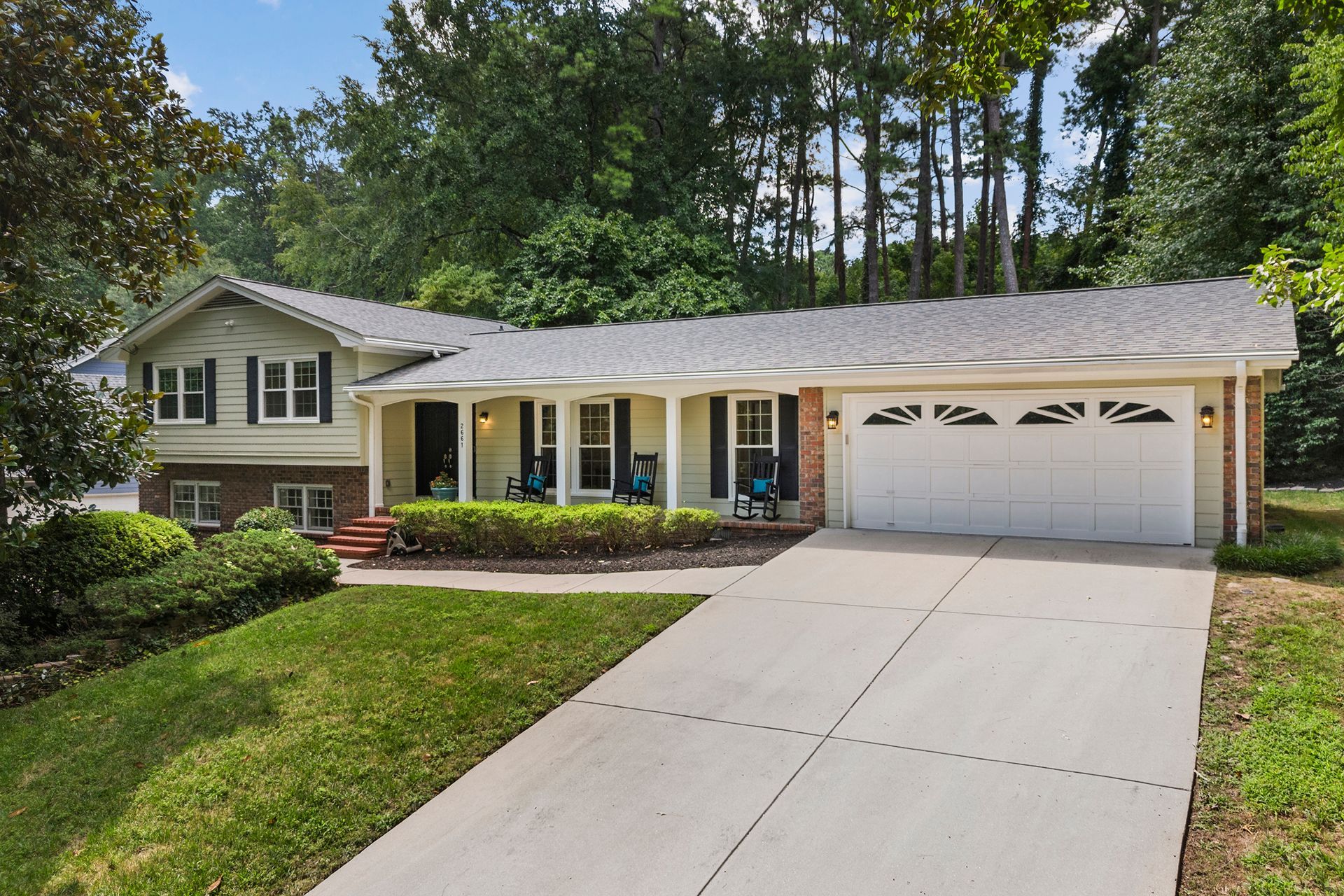 A large house with a large driveway and a porch surrounded by trees.