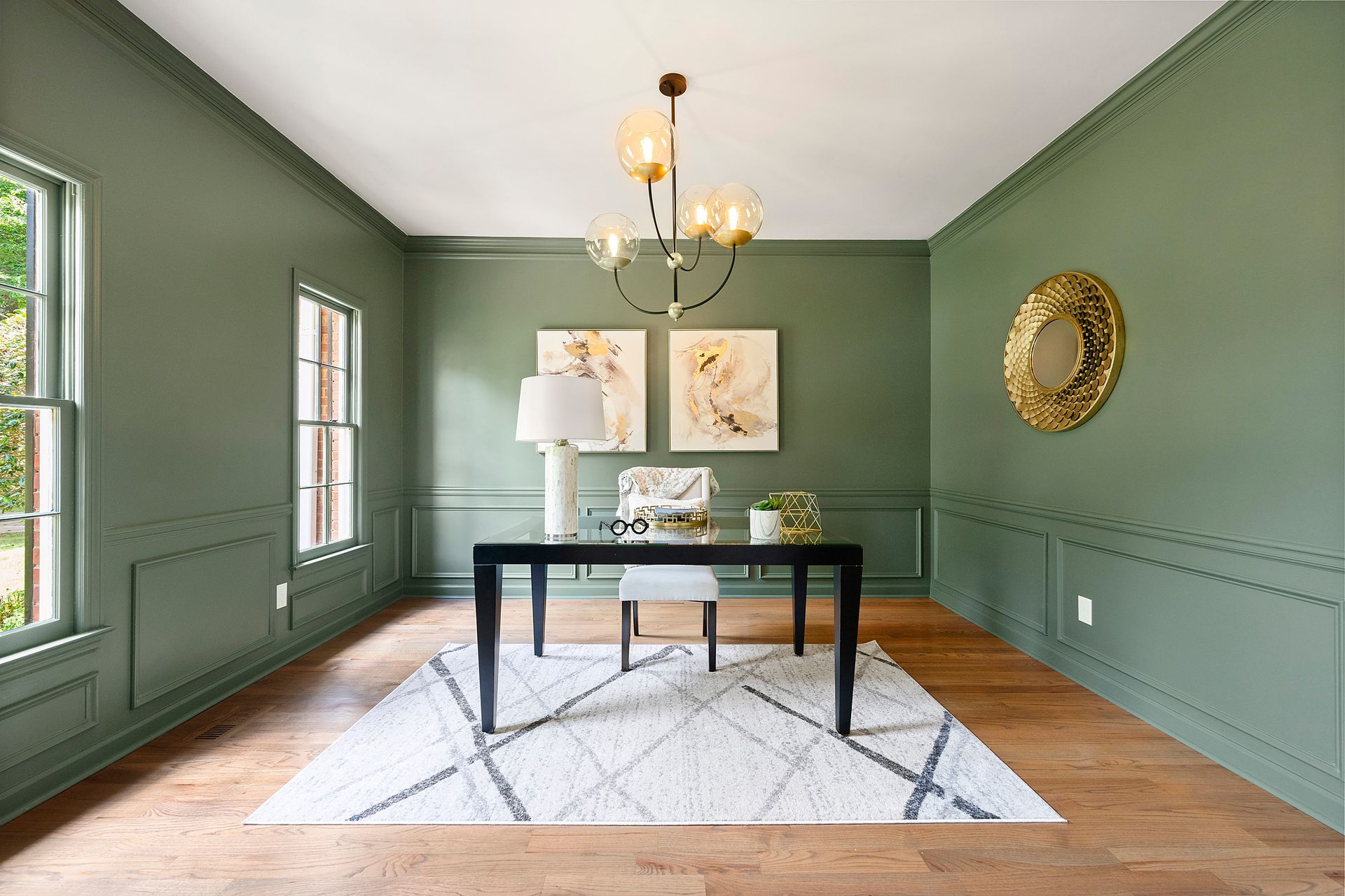 A dining room with green walls , a desk , chairs and a rug.