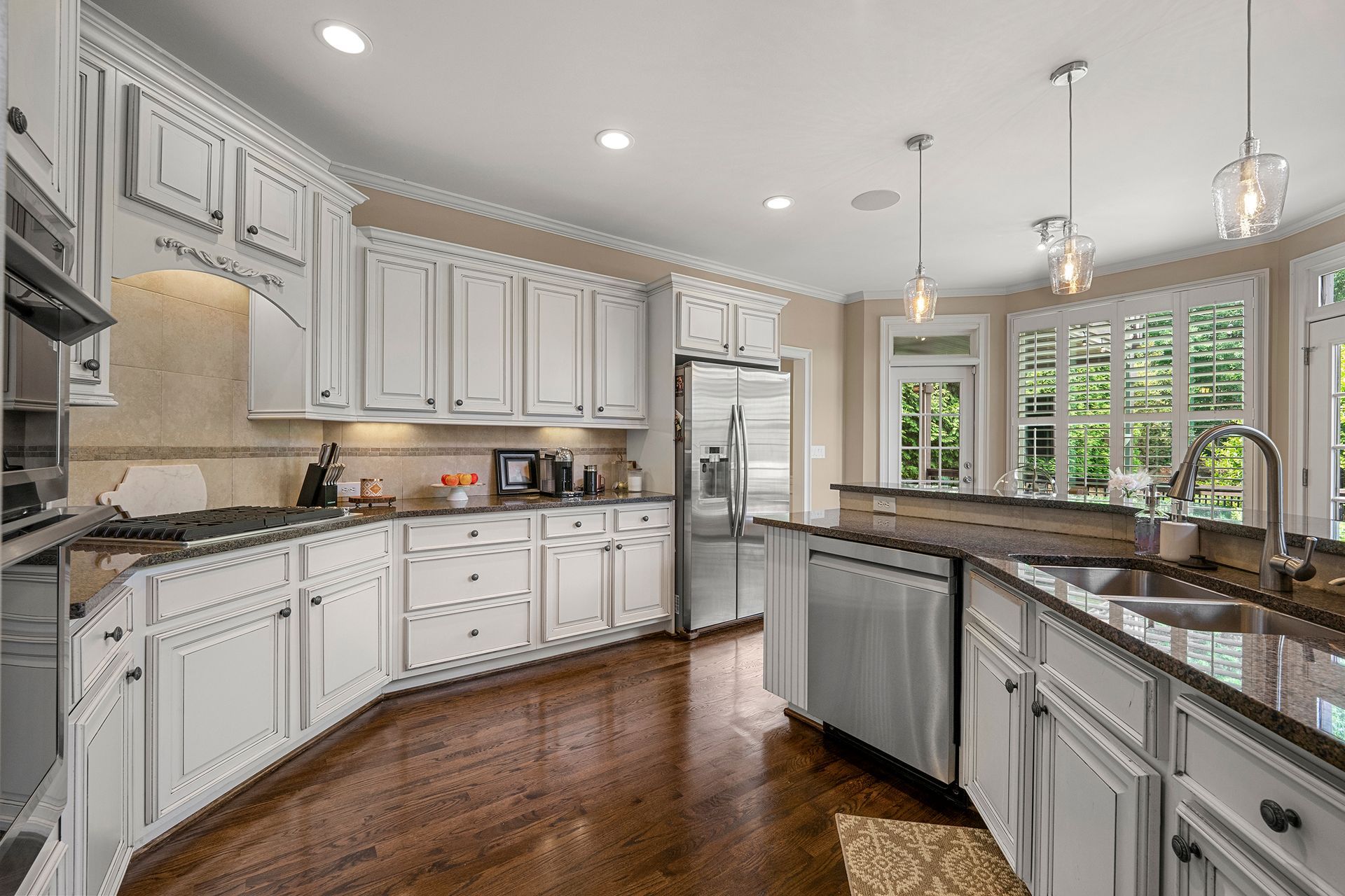 A kitchen with white cabinets , granite counter tops , stainless steel appliances , and hardwood floors.