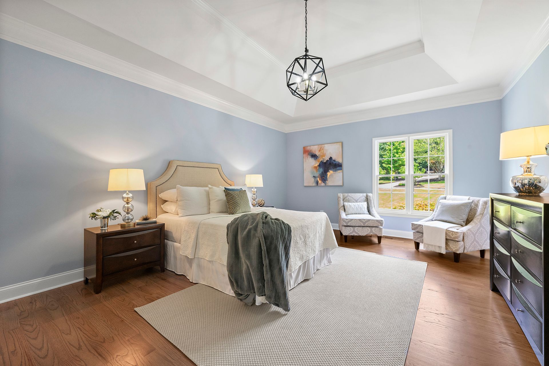 A bedroom with a large bed , two chairs , a dresser , and a chandelier.
