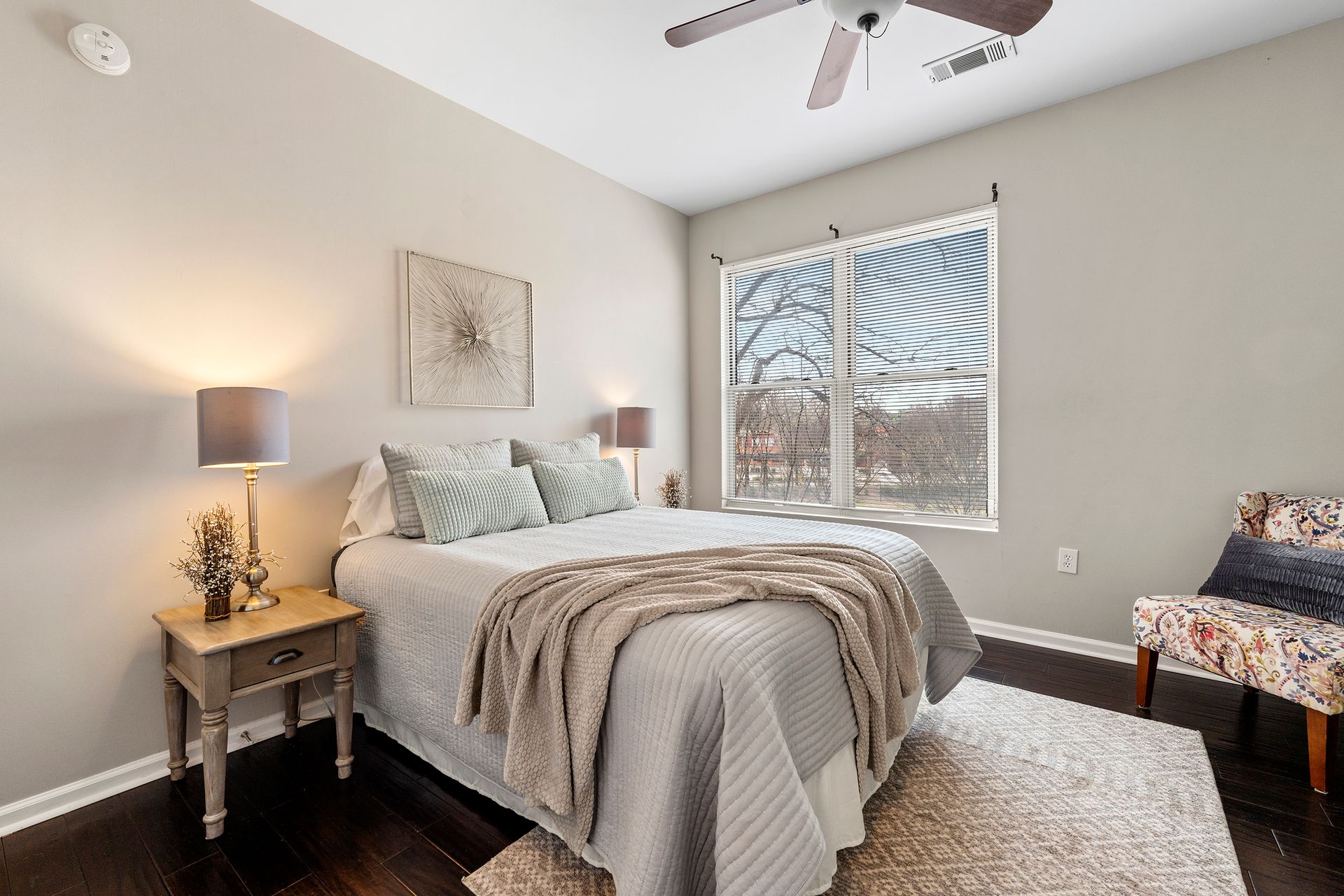 A bedroom with a bed , nightstand , chair and ceiling fan.