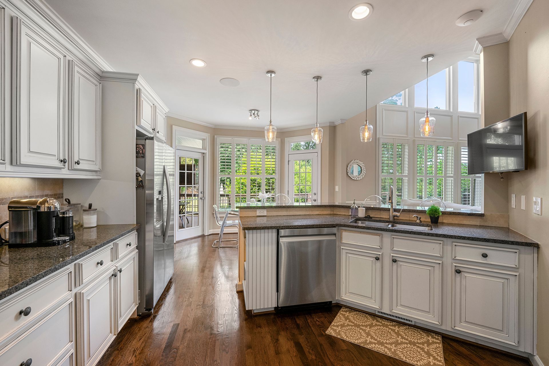 A kitchen with white cabinets , granite counter tops , stainless steel appliances and hardwood floors.