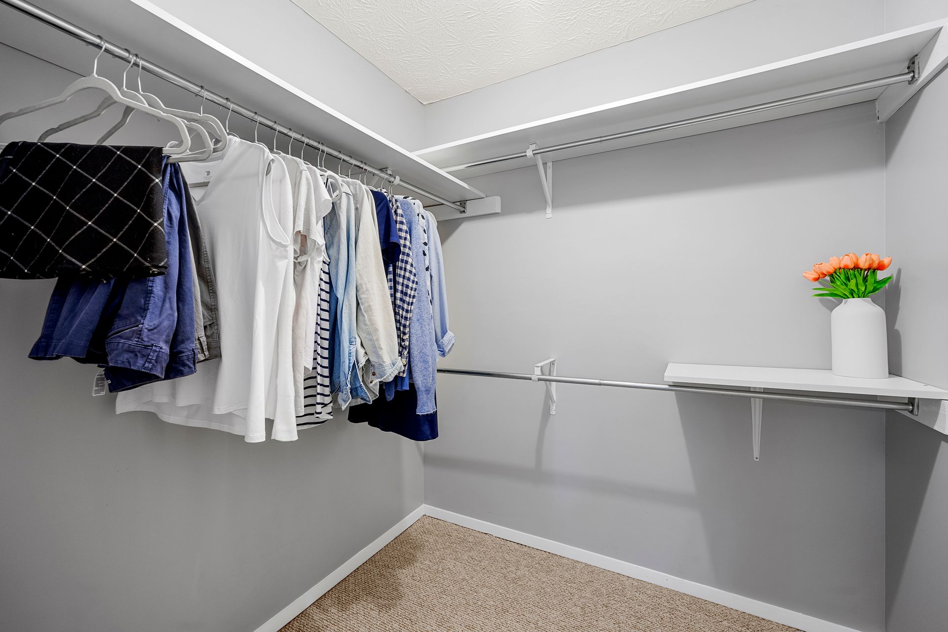 A walk in closet filled with clothes and a vase of flowers.