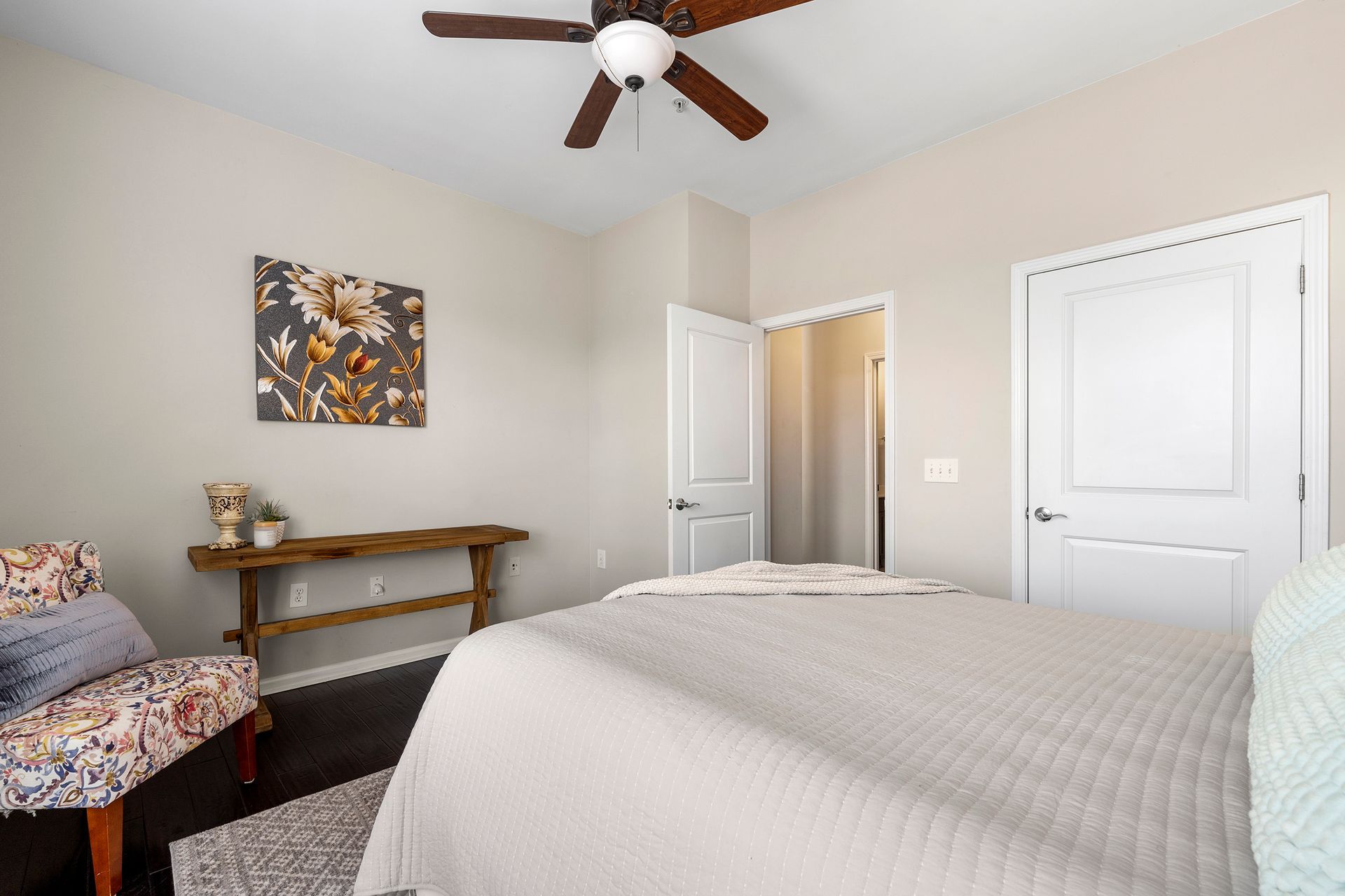A bedroom with a bed , chair , table and ceiling fan.