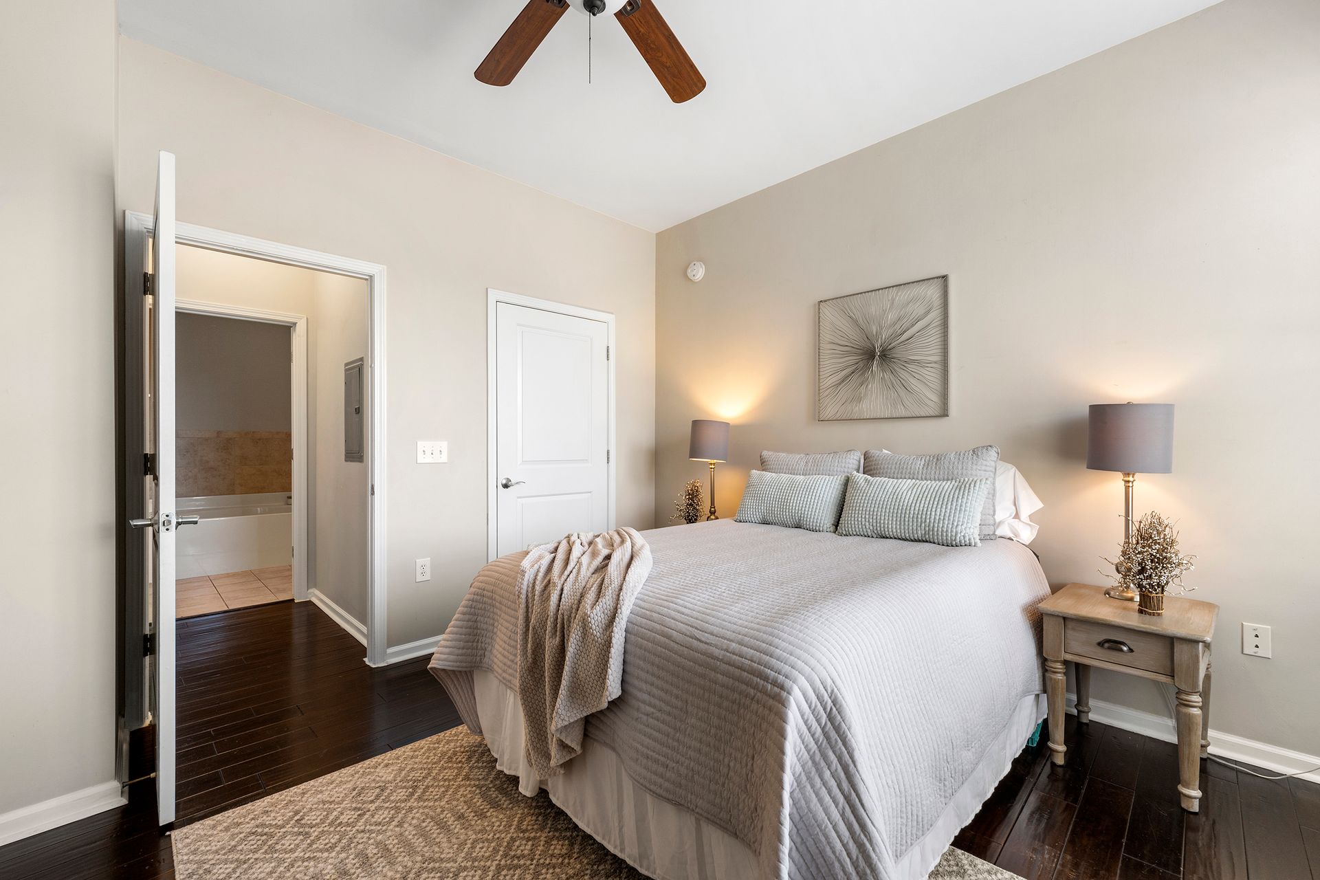 A bedroom with a bed , nightstand , lamps and a ceiling fan.