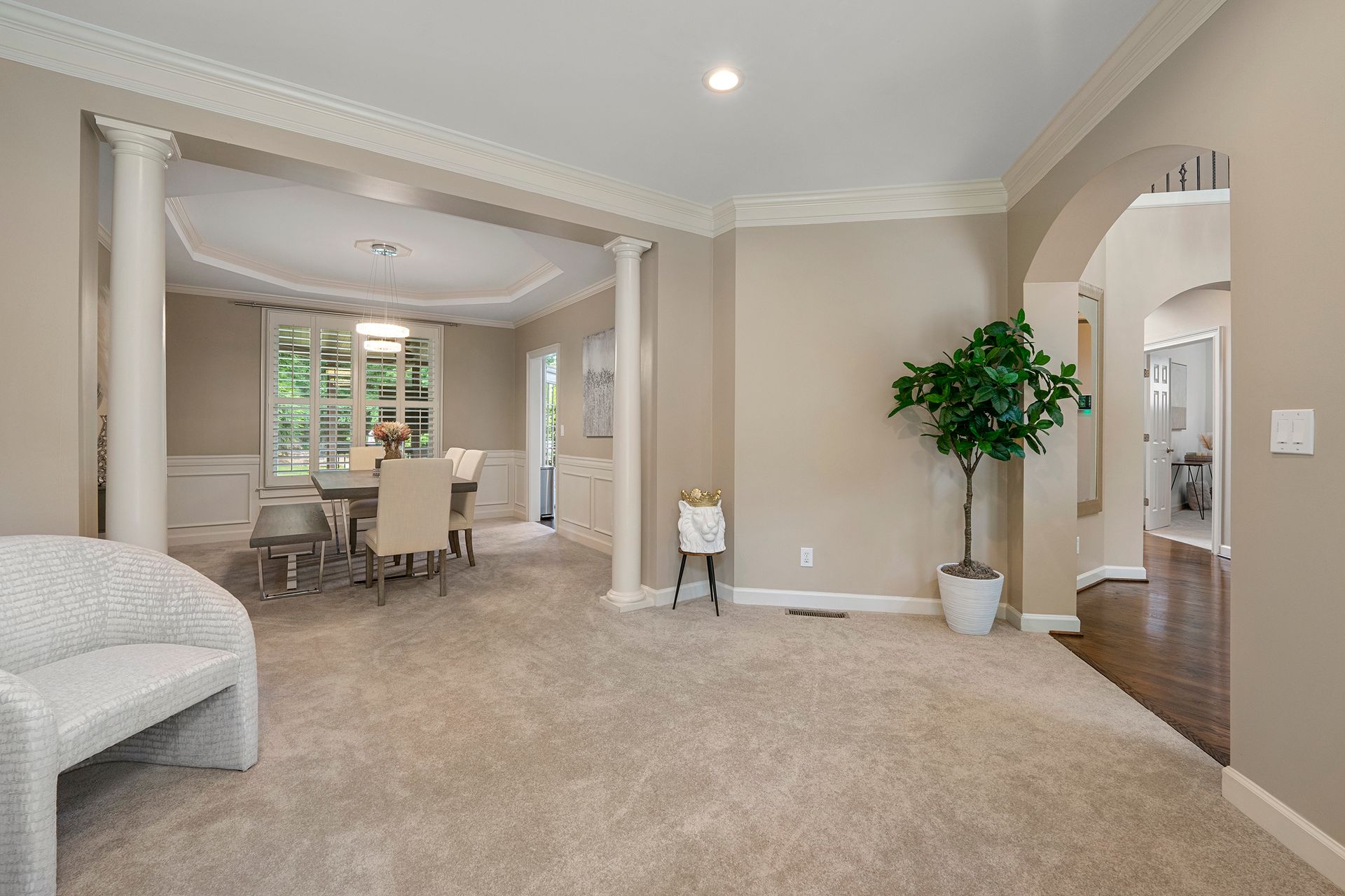 A living room with a dining room table and chairs and a potted plant.