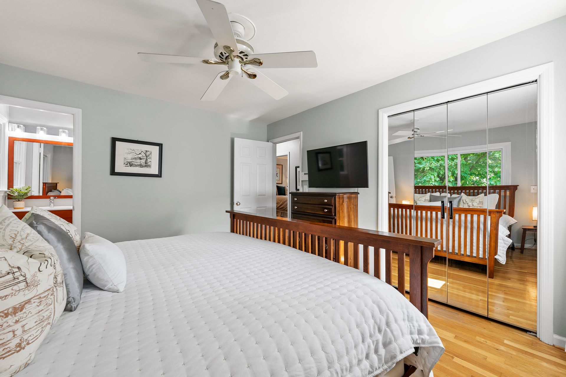 A bedroom with a large bed , a ceiling fan , a television , and a mirrored closet.