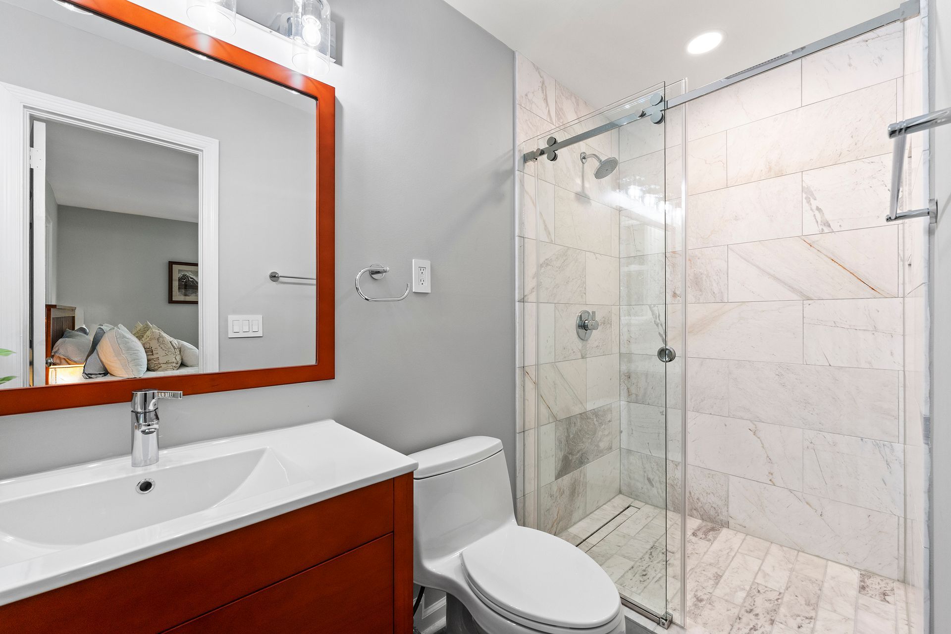 A bathroom with a toilet , sink , mirror and walk in shower.