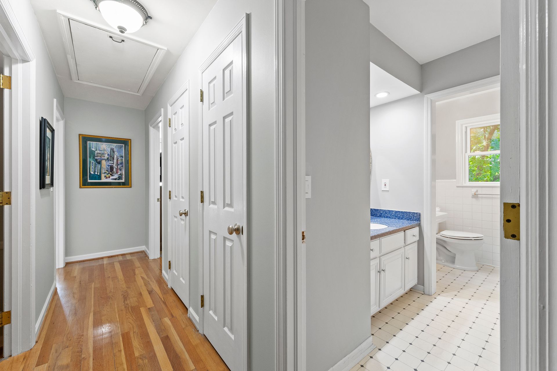 A hallway with hardwood floors and white doors leading to a bathroom.